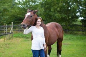 Attractive young pregnant woman and a horse standing in a field